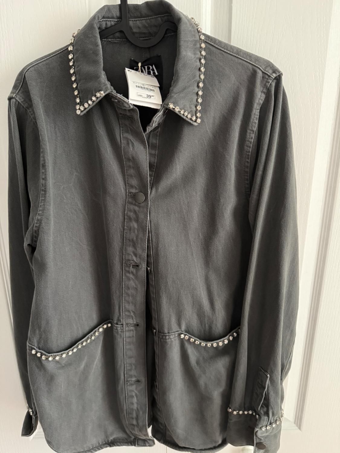 Gray jacket with studs on the collar, pockets, and cuffs, hanging on a hanger. Visible tag with a price of 39.99.