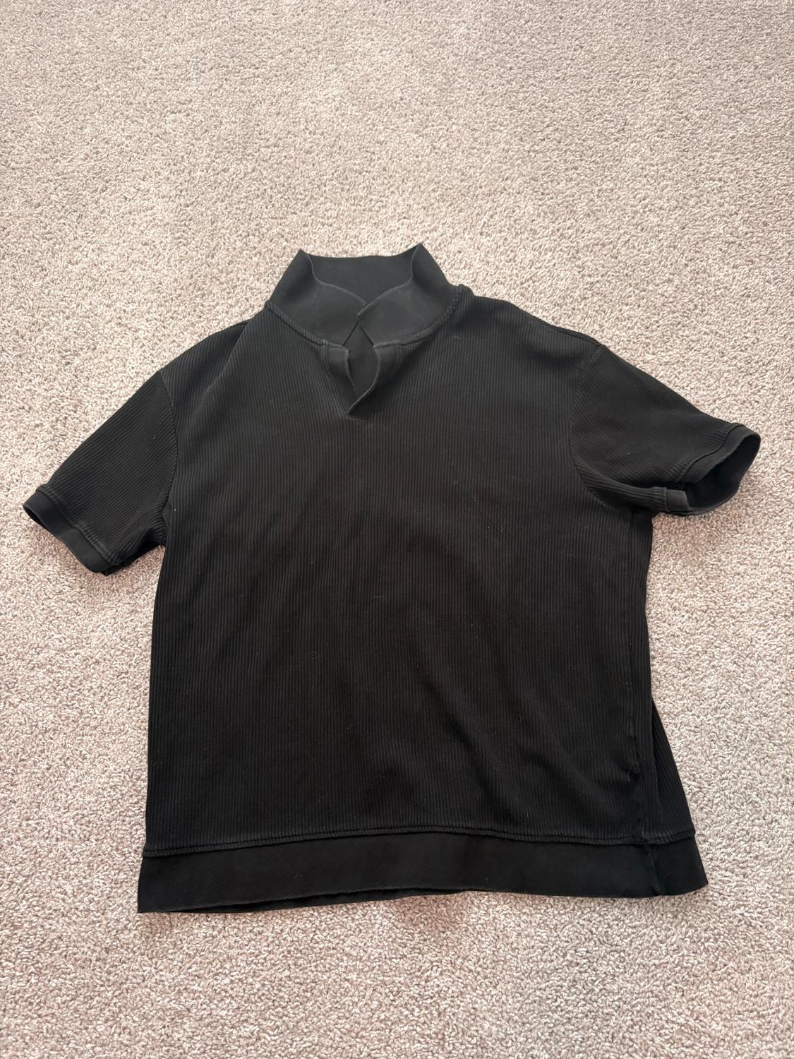 Black short-sleeved turtleneck t-shirt on a beige carpet. Ribbed fabric with a simple design.