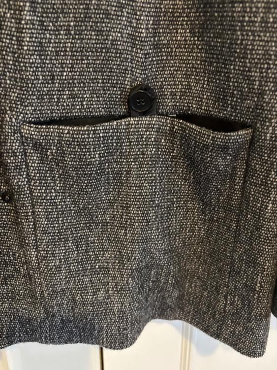 Close-up of a textured grey jacket pocket with a visible black button against a light background.