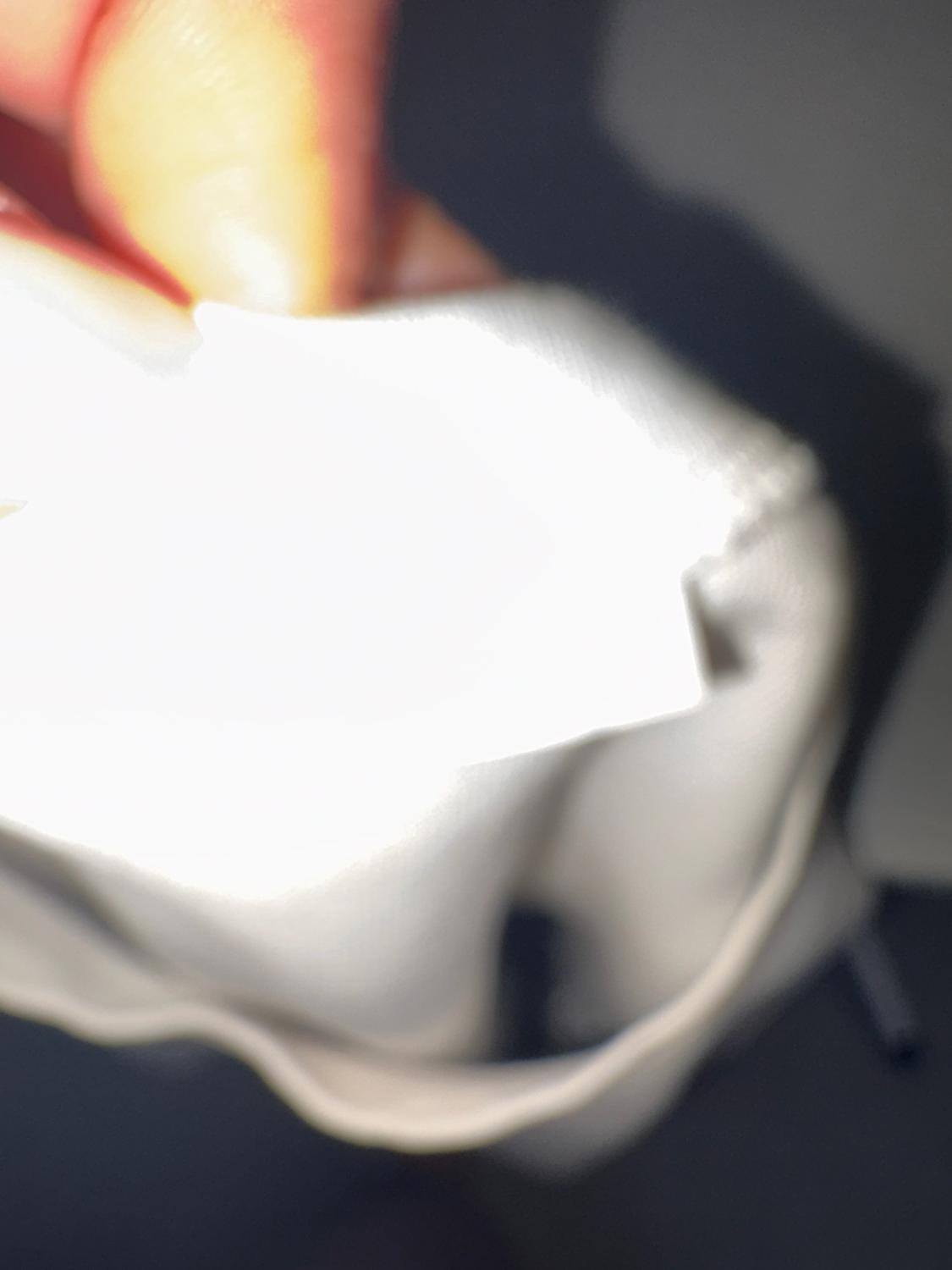 Blurred close-up of fingers holding a brightly lit white fabric against a dark background.