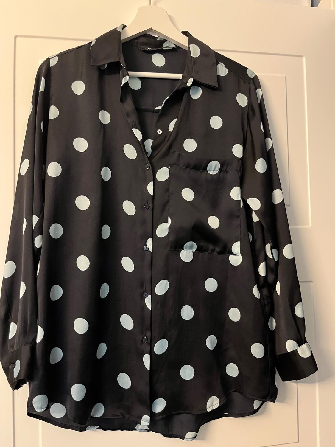 Black shirt with white polka dots hanging on a white hanger over a white door.