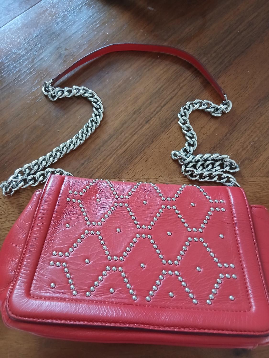 Front view of a red handbag with a silver chain and diamond-shaped studs.