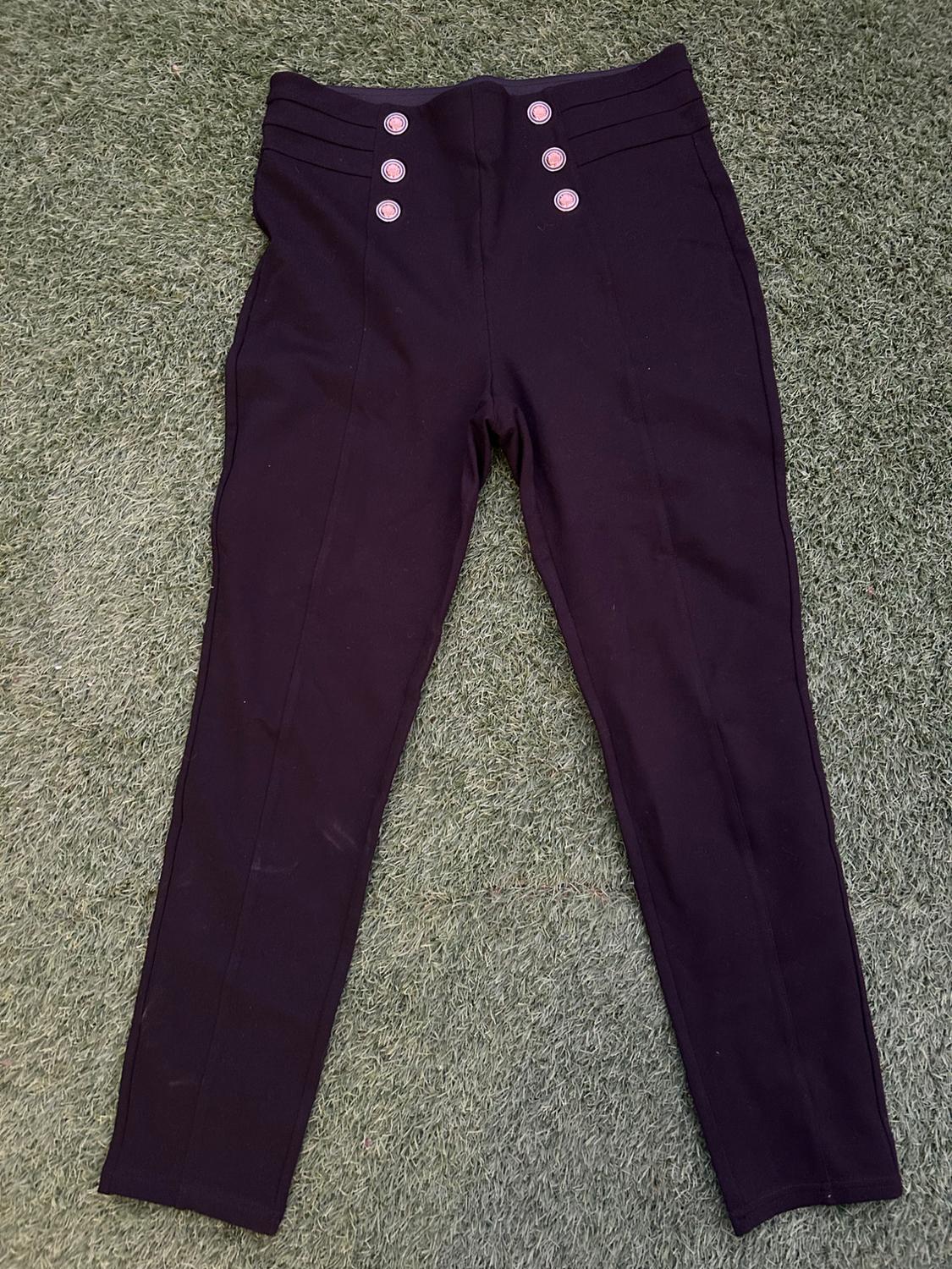 Black trousers with gold buttons on the waistband, laid out on green grass.