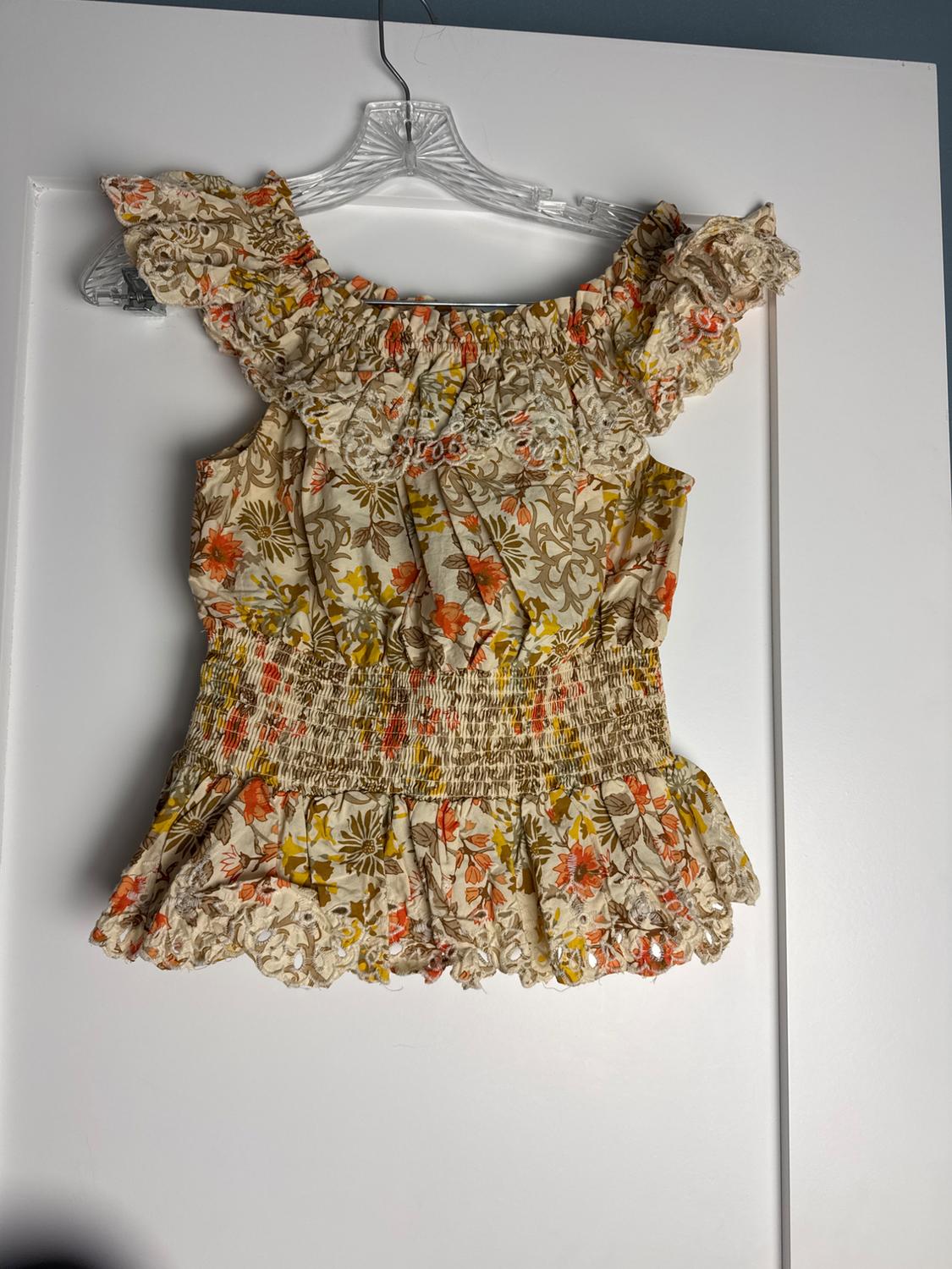 Top floral with ruffles, shirred elasticated waist and cut-out details, hanging on a clear hanger over a white door.