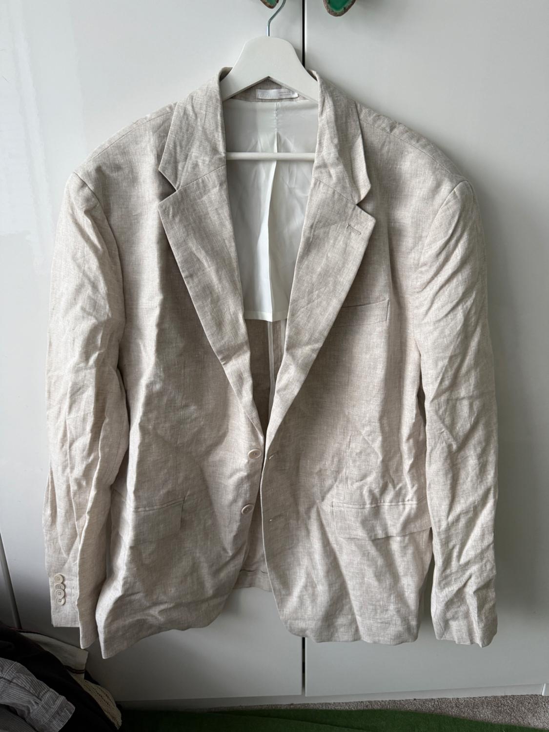 Creased beige jacket hanging on a white hanger in front of a white wardrobe.