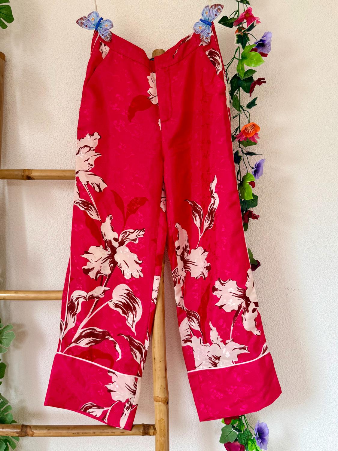 Red trousers with a white floral print hanging on a bamboo ladder, decorated with artificial butterflies and flowers.