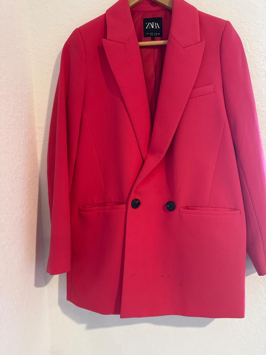Red double-breasted jacket hanging on a wooden hanger. Visible label with the text "ZARA". White background.