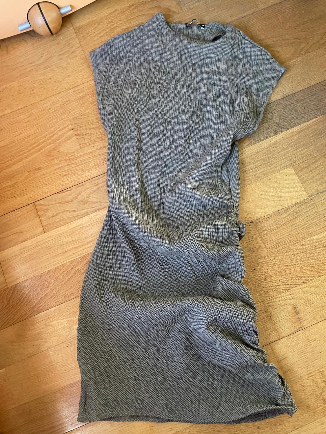 Textured grey short-sleeved dress on a light wood floor. Background with part of a piece of furniture and a ball.