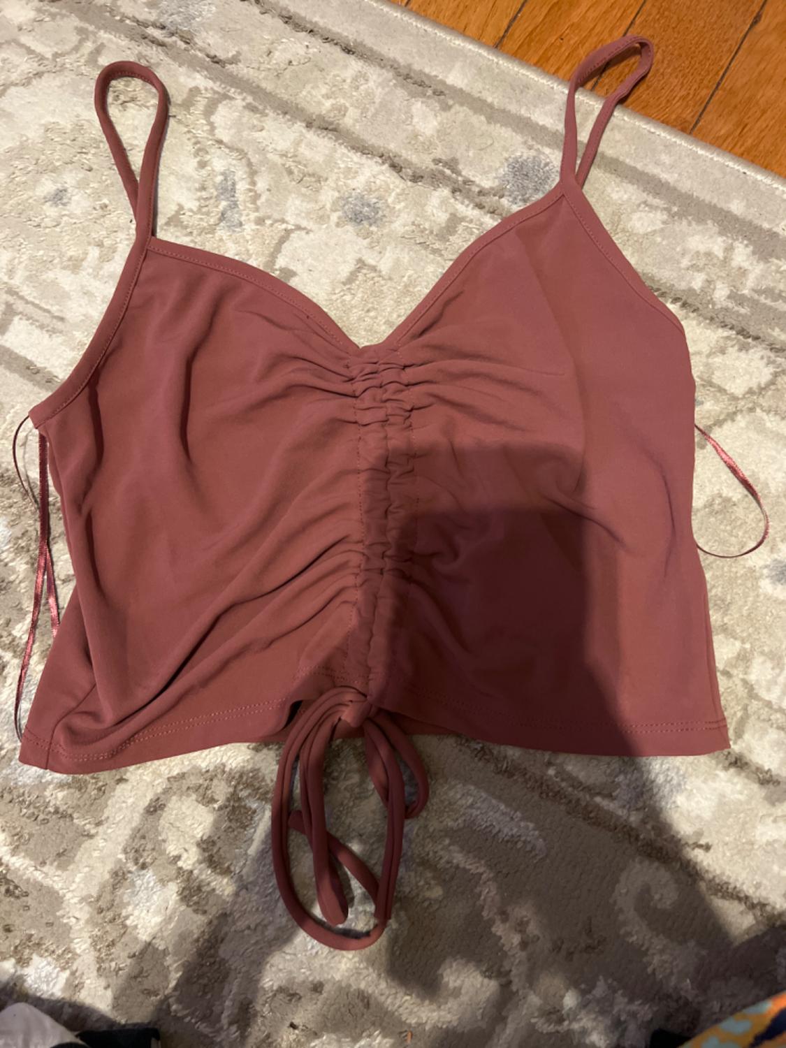 Cropped reddish-brown top with thin straps and adjustable ruching detail at the center, on a beige rug with textured design.