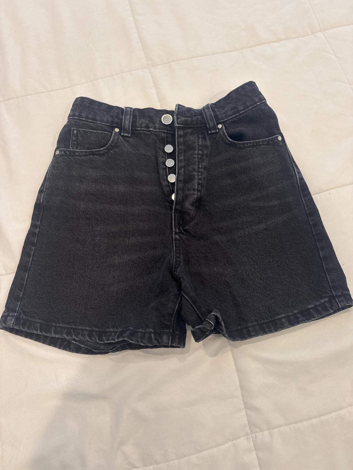 Black denim shorts with metal buttons on the front, on a white quilt.