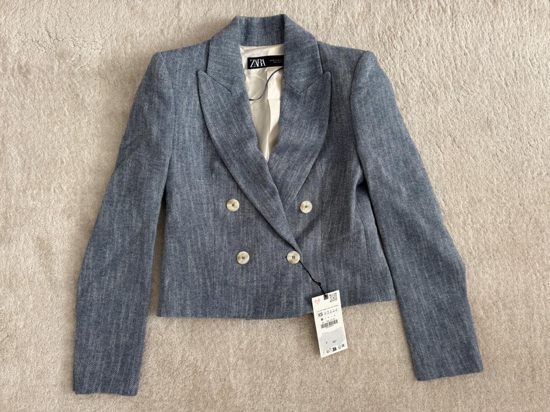 Blue double-breasted jacket with Zara tag, on a beige background. Elegant and modern design, size XS visible on the tag.