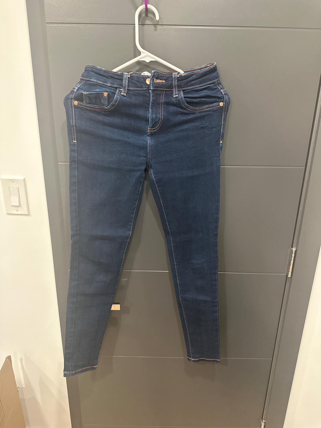 Dark blue jeans hanging on a white hanger over a gray door. Front pockets and visible seams.