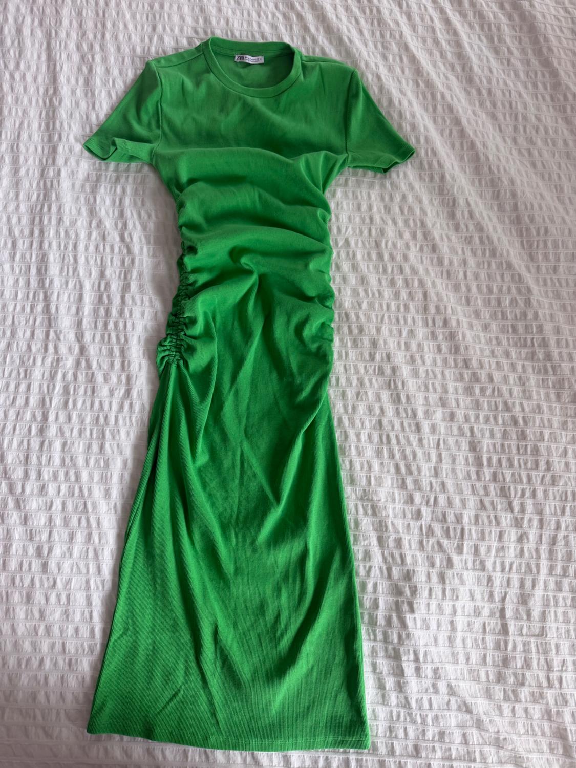 Green short-sleeved, round-neck dress with side ruching, casually displayed on a white sheet.