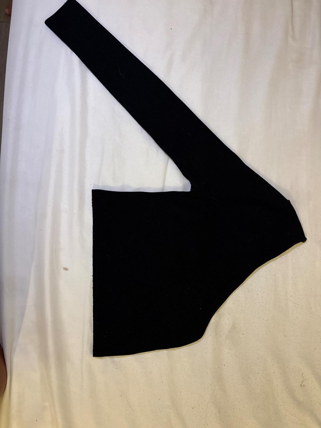 Black asymmetric cropped top with a single long sleeve, laid out on a crumpled white sheet.