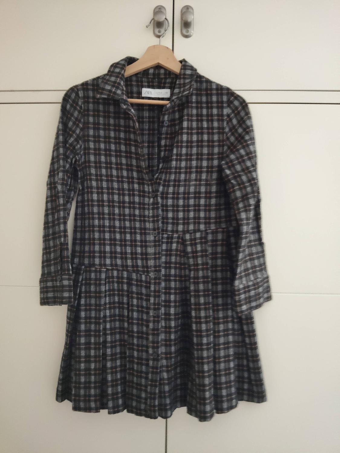 Dark-toned checked dress hanging on a wooden hanger in front of a white wardrobe.