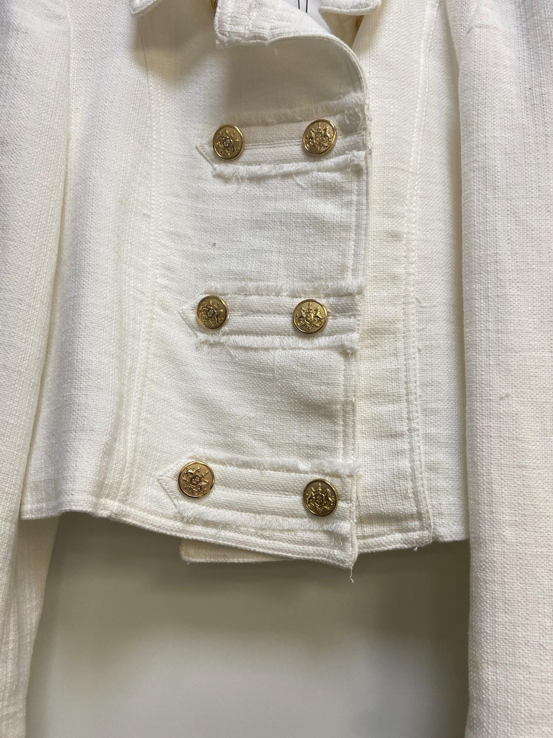 Close-up of a white textured jacket with raised gold buttons and frayed edges.