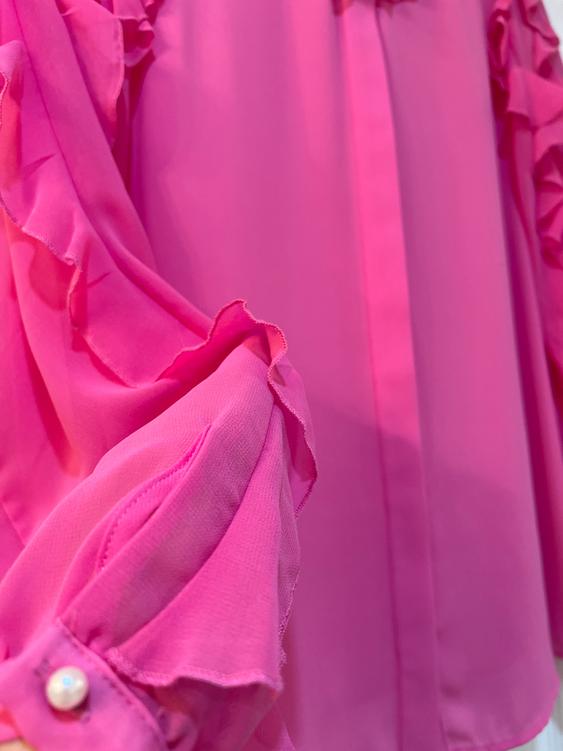 Pink blouse with ruffled sleeves and buttoned cuffs, featuring light and flowy fabric.