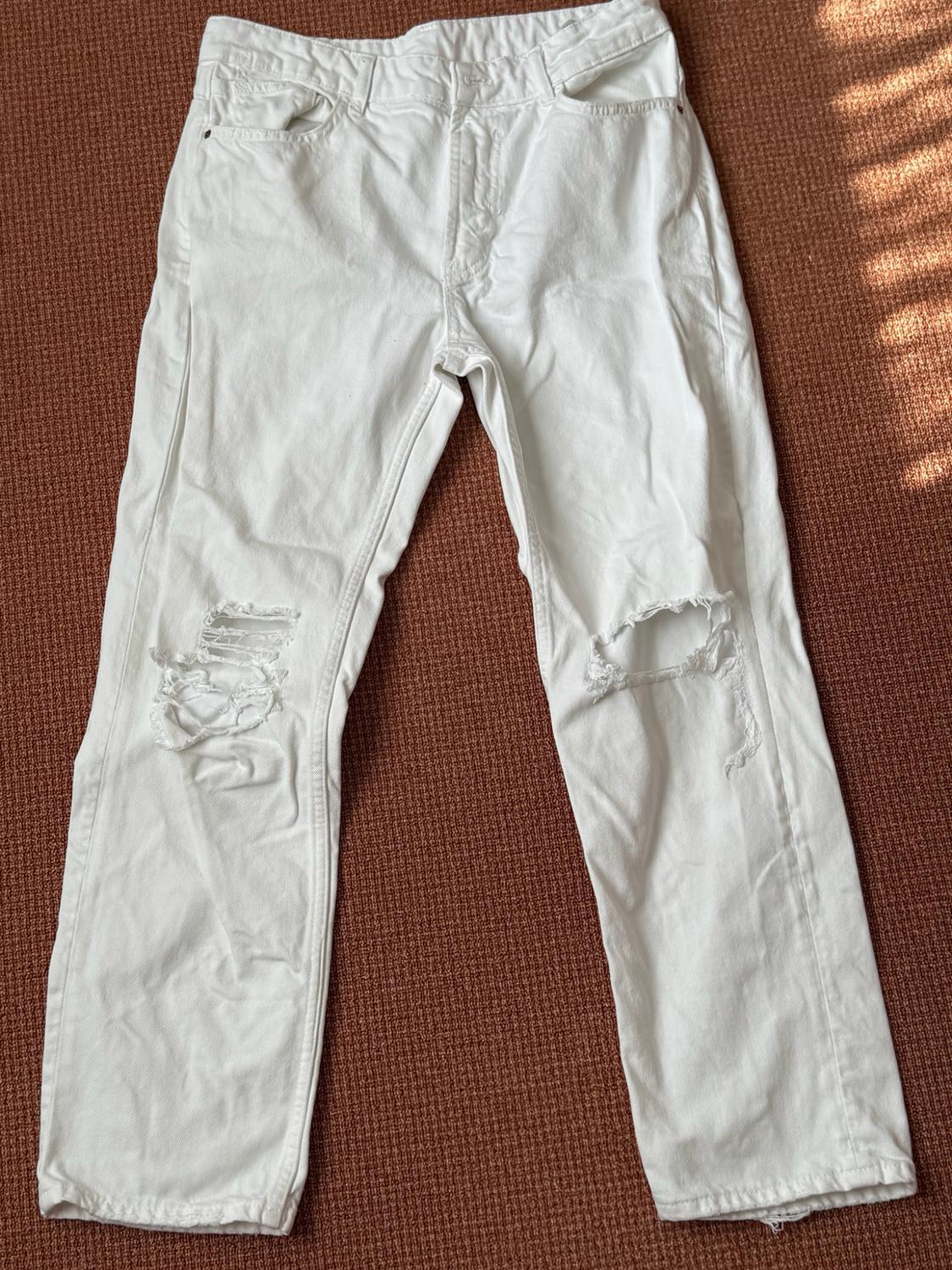 White jeans with rips at the knees, laid out on a textured terracotta-coloured background lit by natural light.