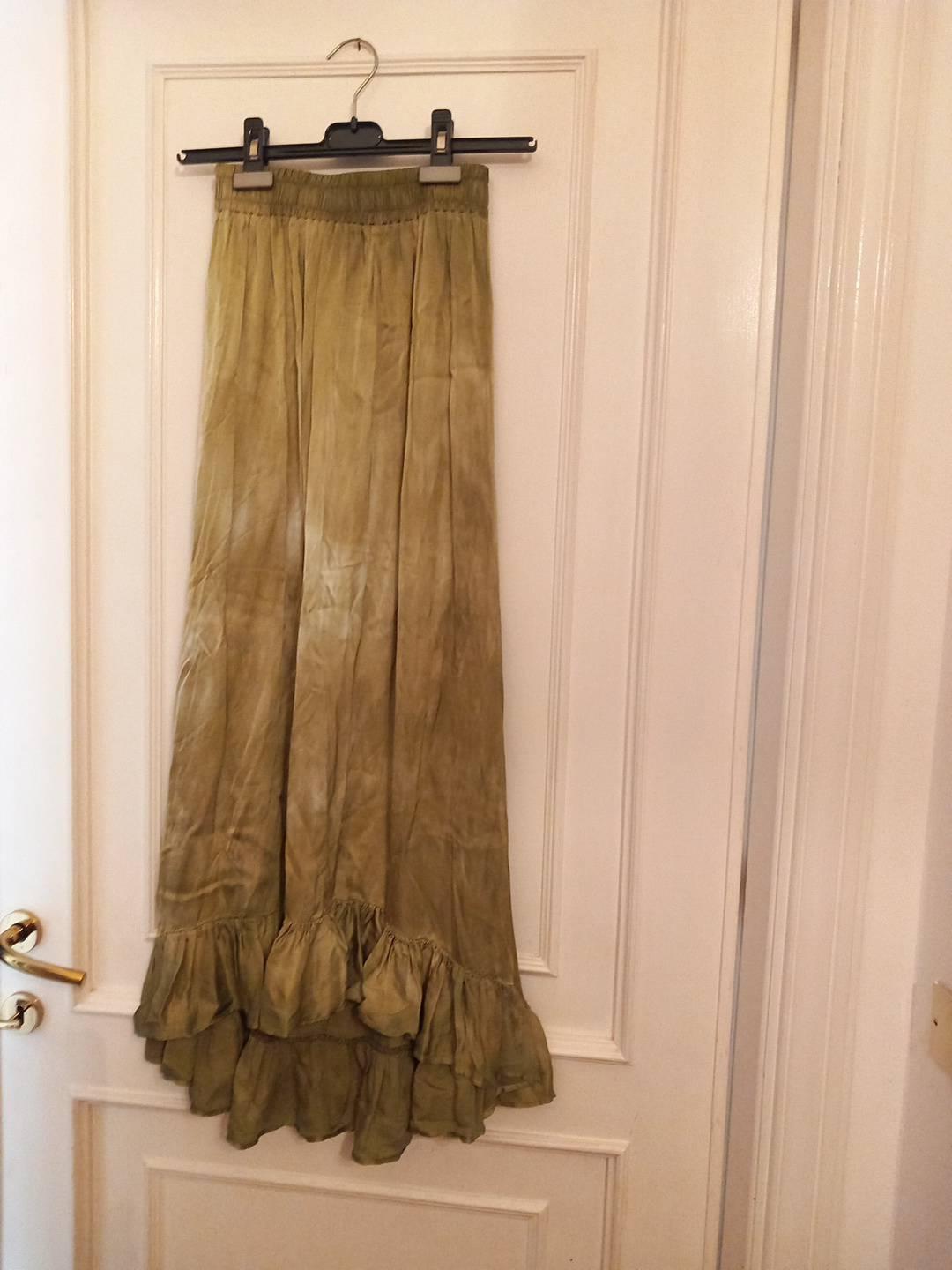Olive green maxi skirt with an elasticated waistband and a ruffled hem, hanging from a black hanger on a white door with a gold handle.