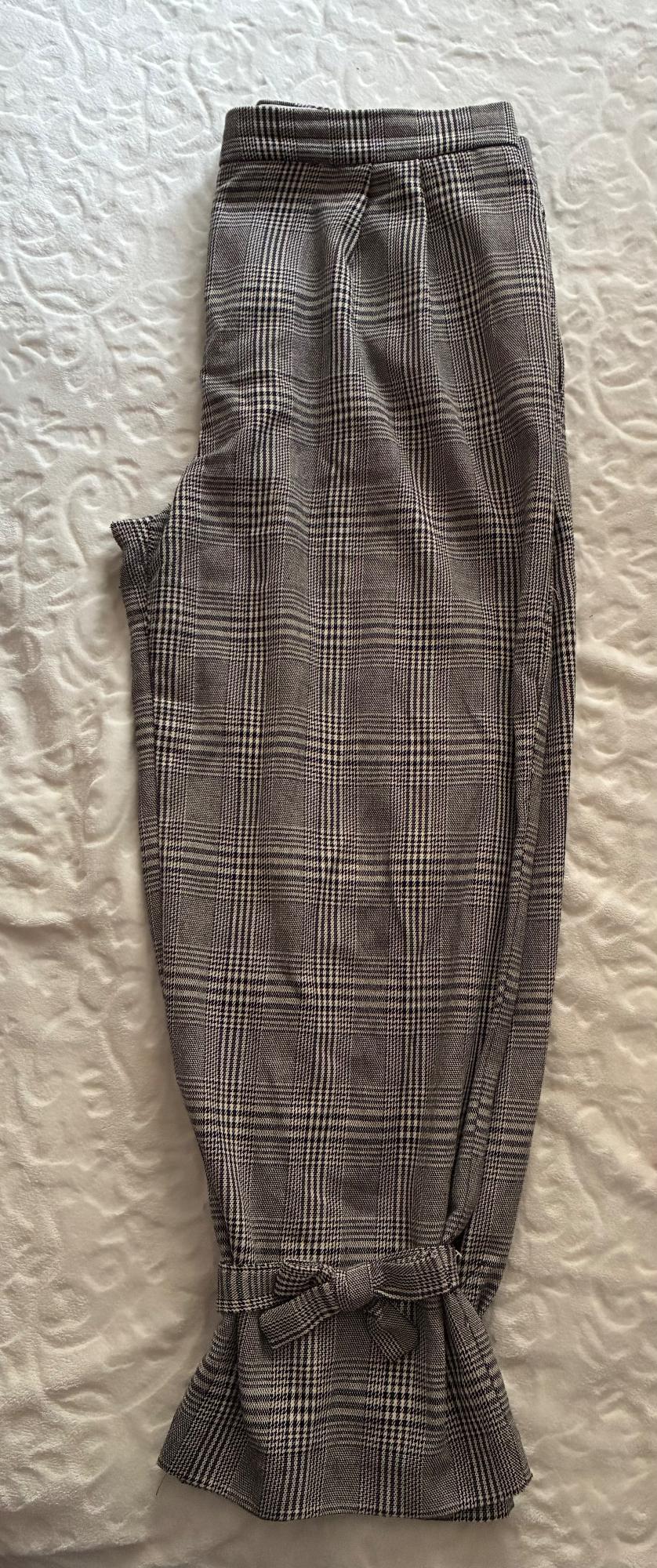 Grey checked trousers with a bow at the ankle, on a textured white surface.