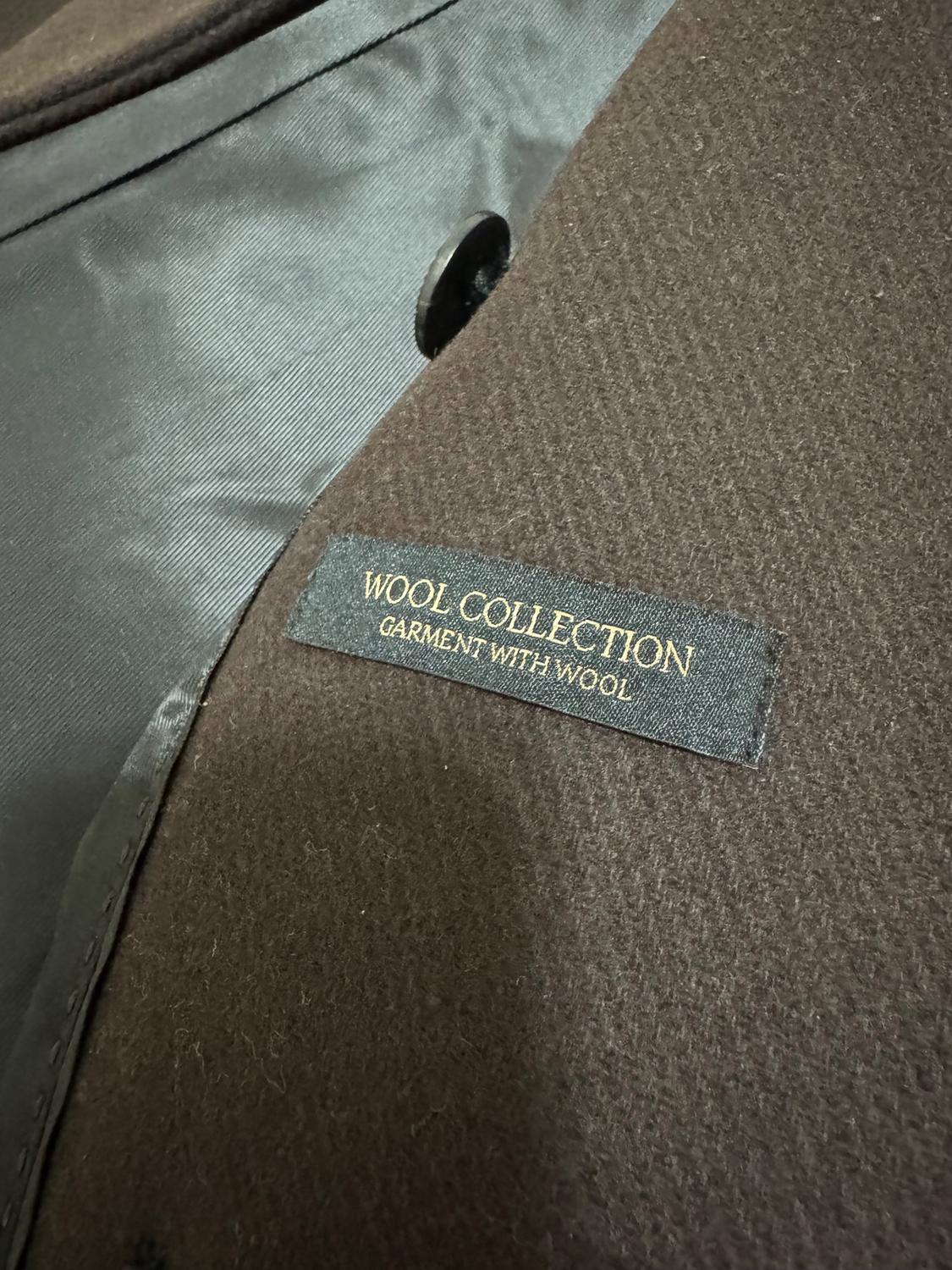 Label on a brown coat that says "WOOL COLLECTION GARMENT WITH WOOL." Black inner fabric visible next to a black button.