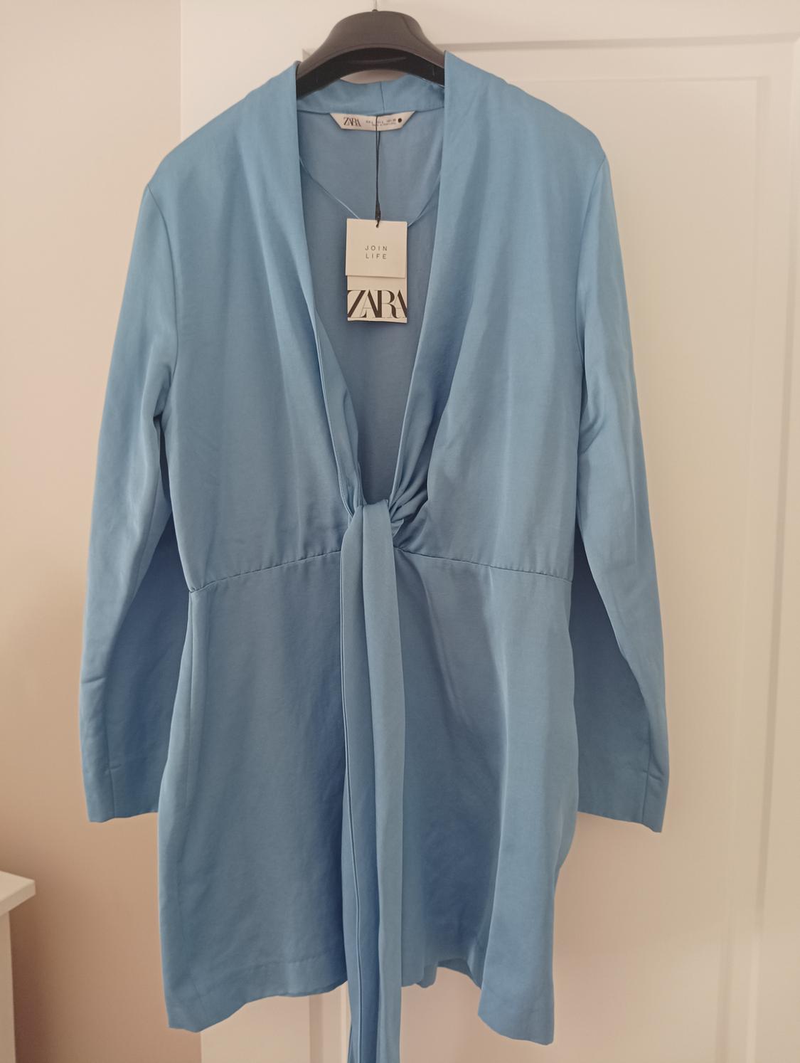 Light blue dress with a front bow, hanging on a black hanger. Visible label with "JOIN LIFE" and "ZARA" text. White background.