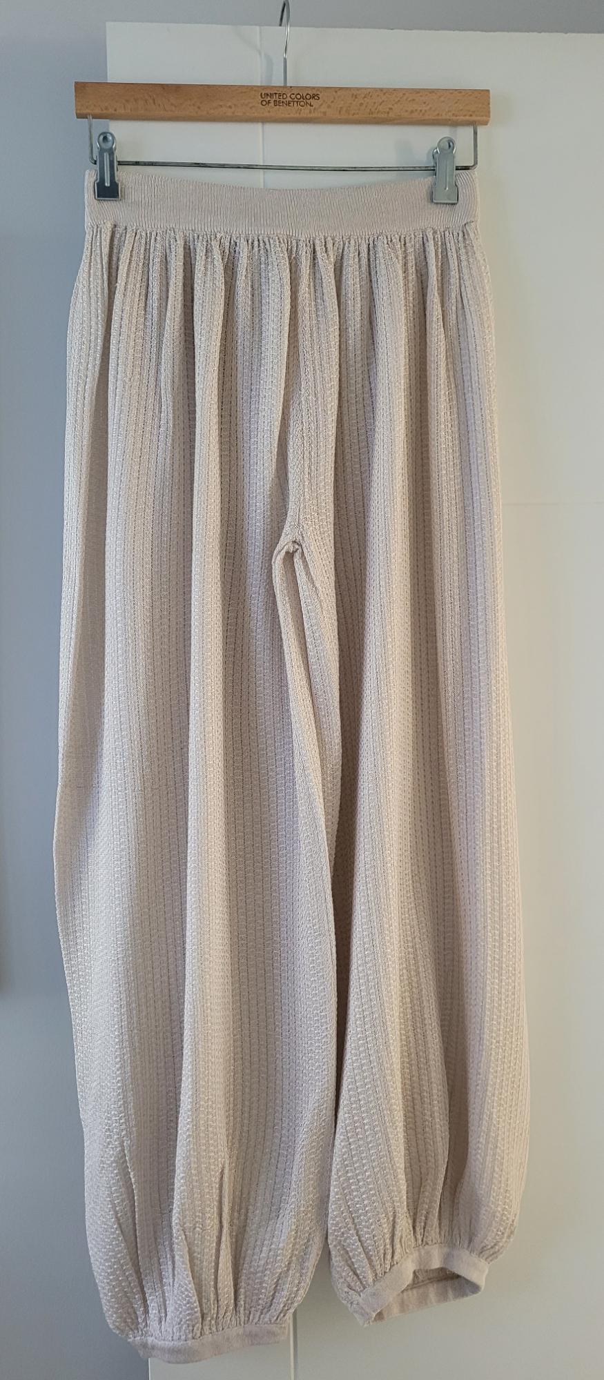 Beige textured fabric trousers hanging on a wooden hanger with the "United Colors of Benetton" brand visible.