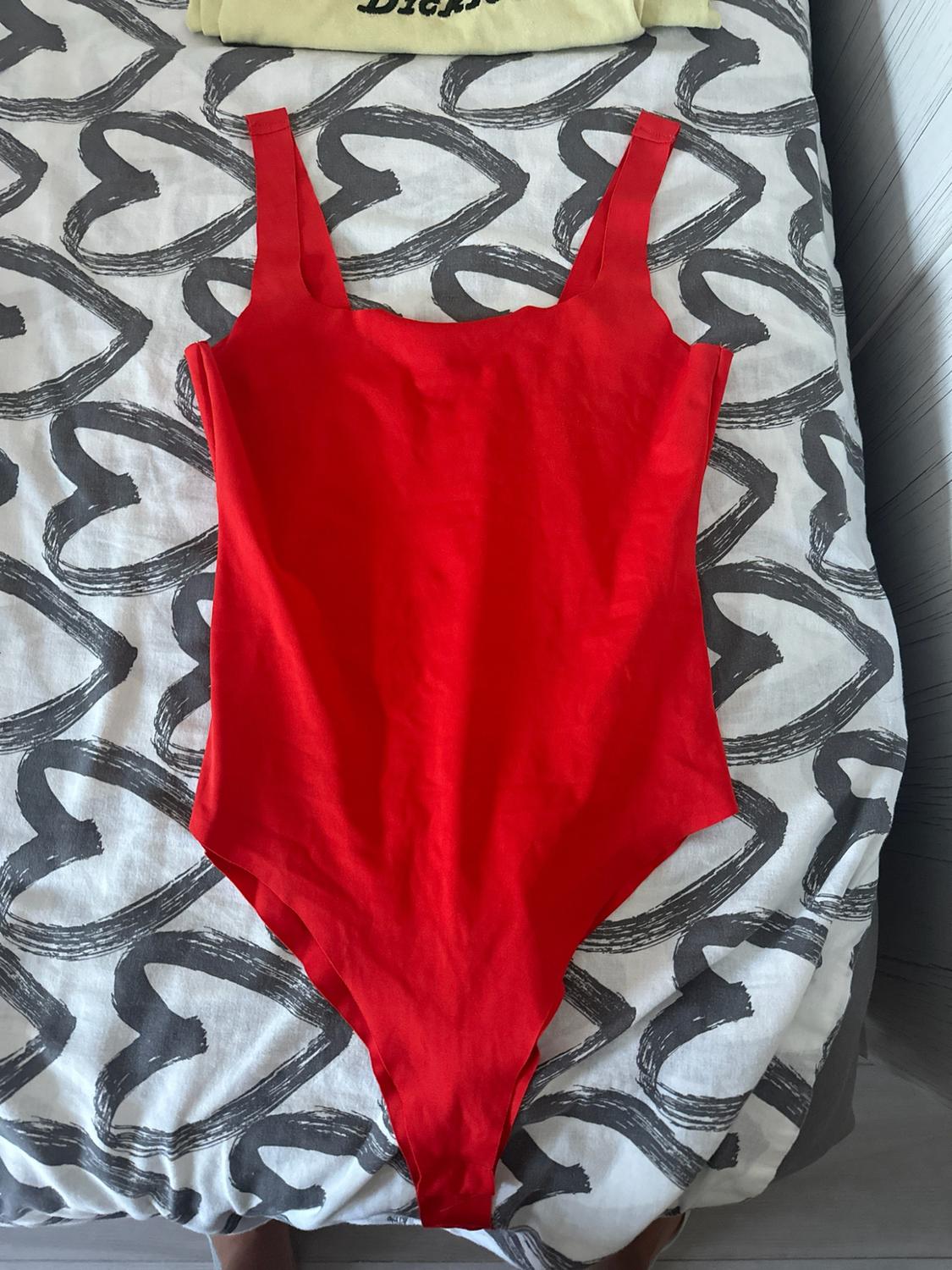 Red strap bodysuit on a bed with white sheets featuring a grey heart print.