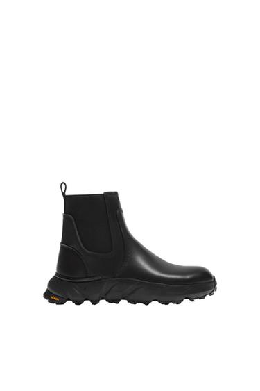 Black leather boot with a thick sole and "Vibram" brand detail on the bottom, on a white background.