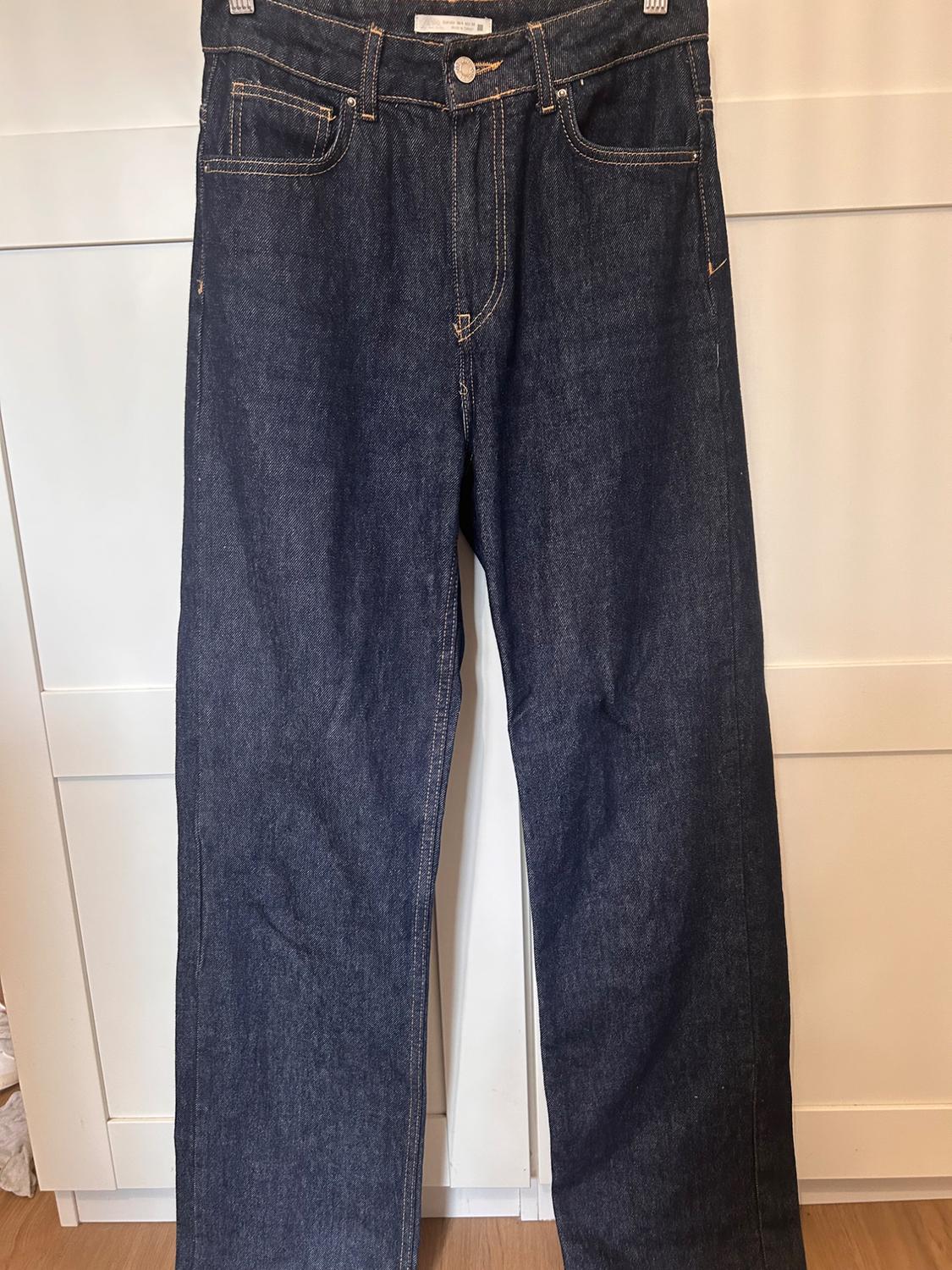 Dark blue denim jeans hanging on a white door, with visible seams and five pockets.