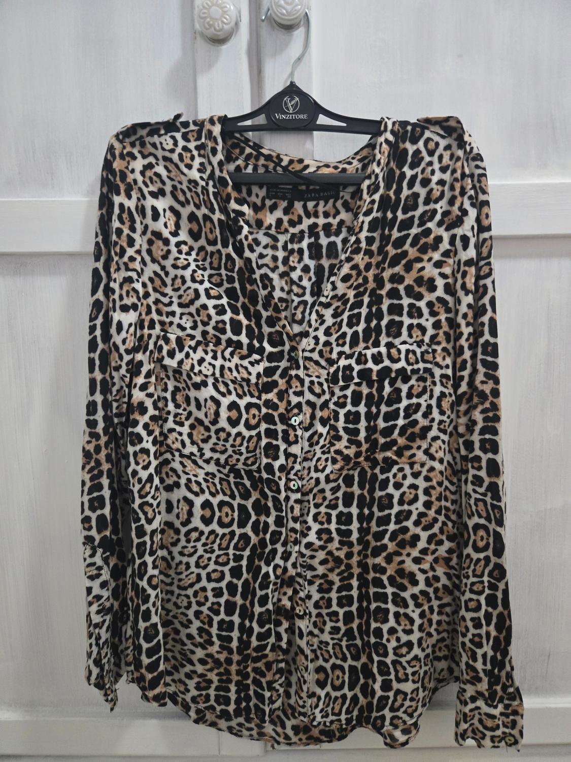 Πουκάμισο με animal print κρεμασμένο σε μια μαύρη κρεμάστρα με την επωνυμία "Vinzitore", πάνω σε φόντο από λευκές πόρτες.
