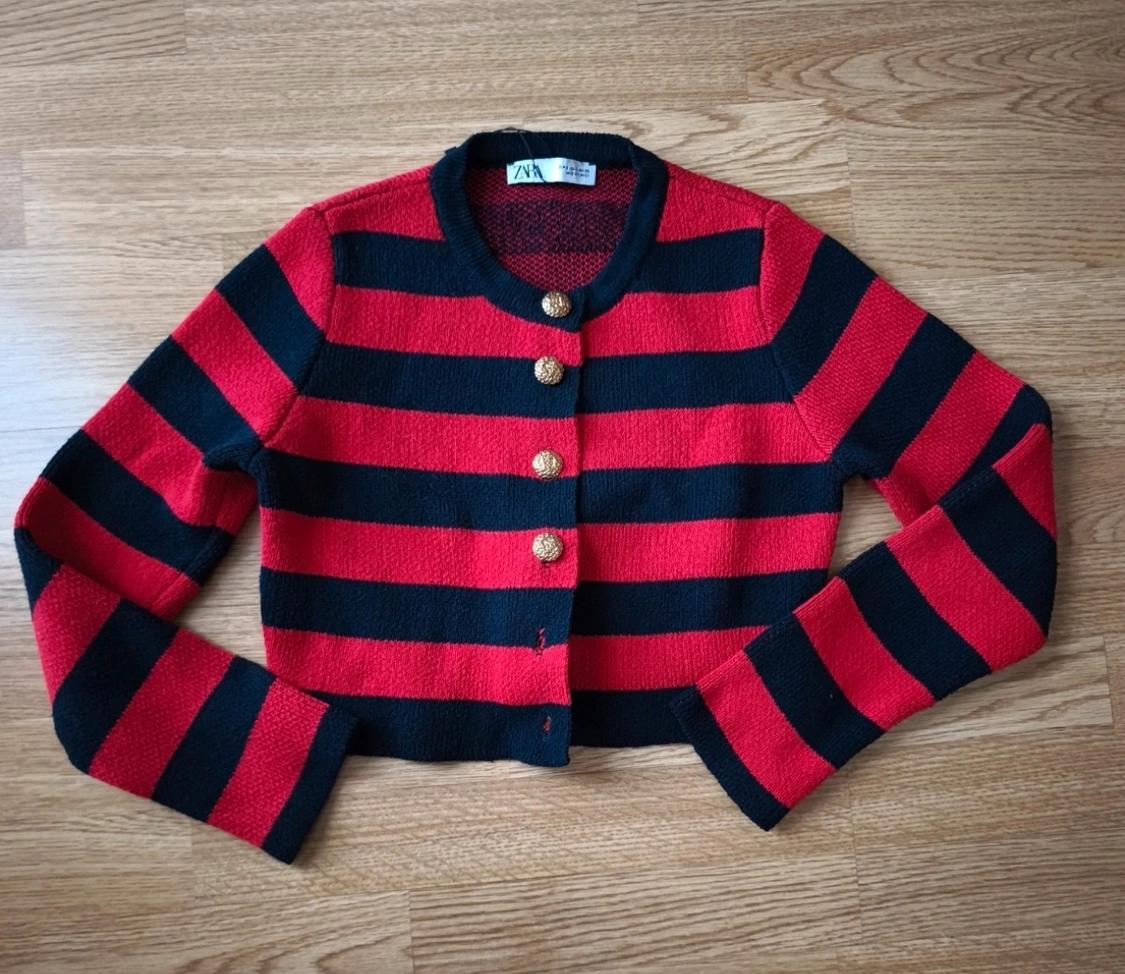 Red and black striped knit jacket with gold buttons on a light wooden floor. Visible label on the collar.