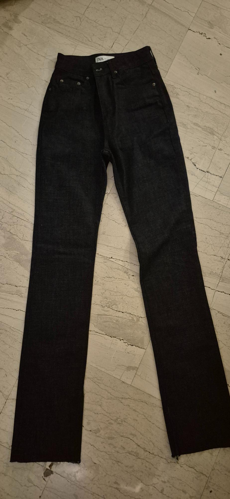 Dark denim jeans on a light marble floor. Visible label on the waistband with the text "ZARA".