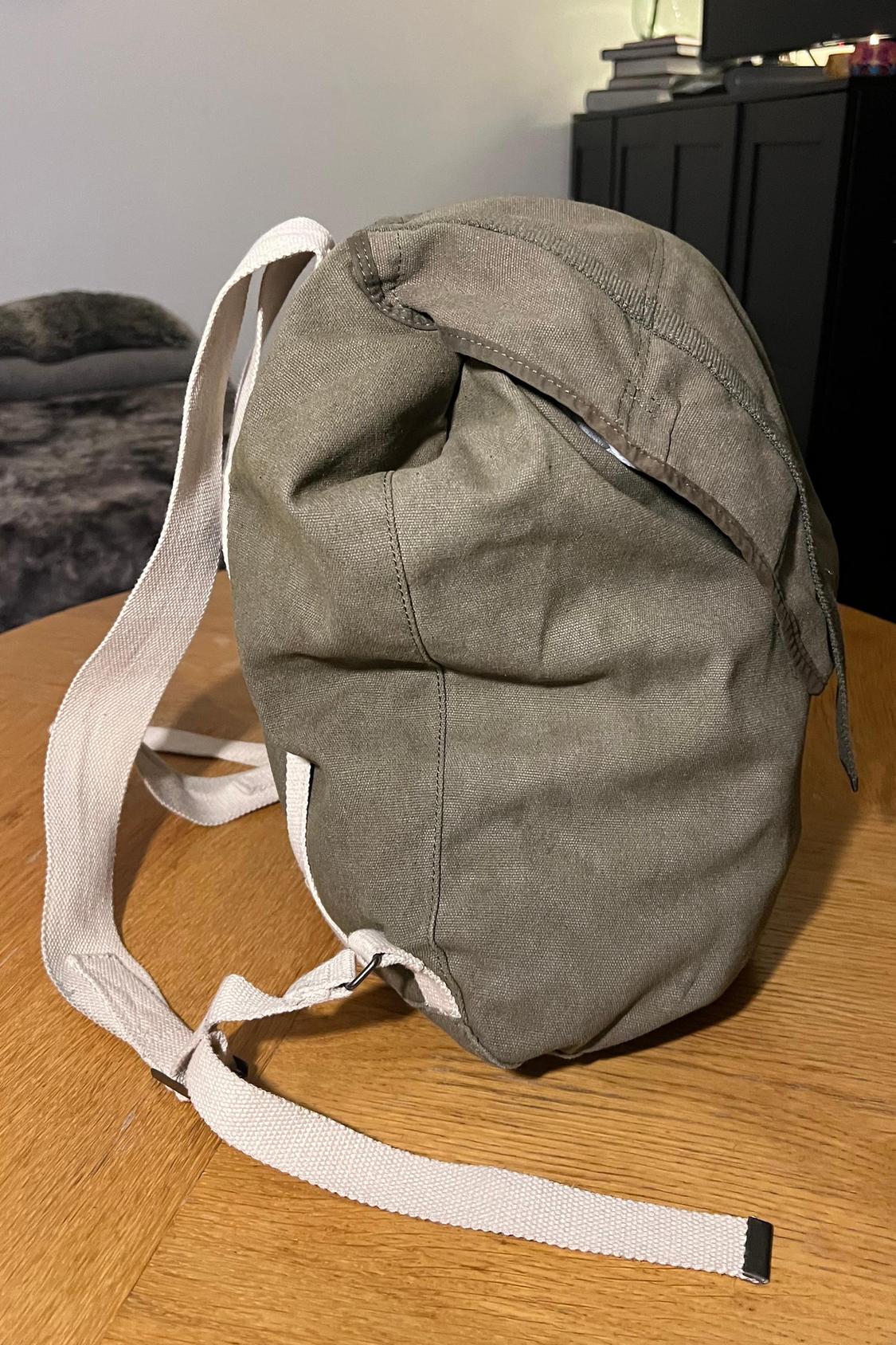 Side view of olive green rucksack with white straps on wooden table.