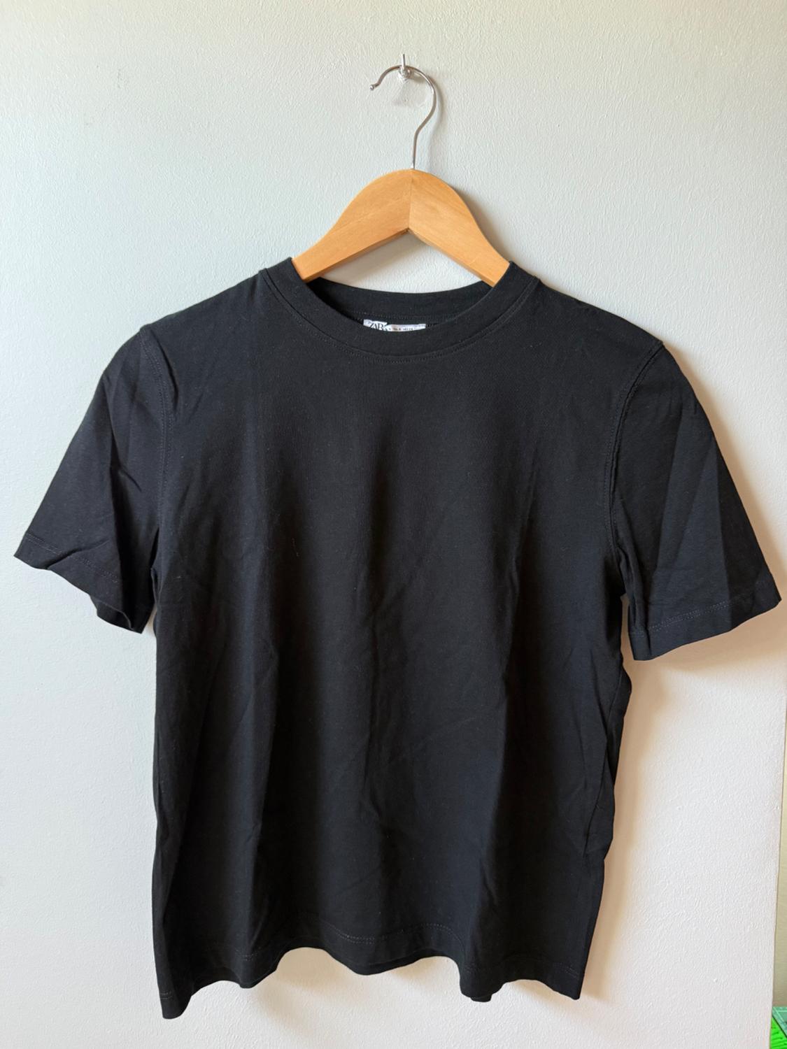 Black short-sleeved t-shirt hanging on a wooden hanger against a white background.