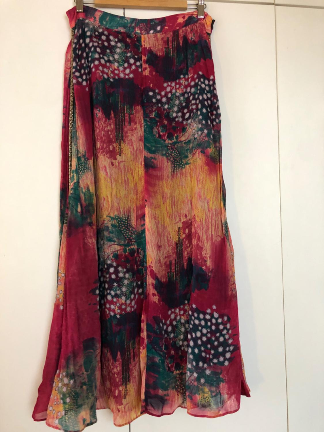 Long skirt with an abstract print in shades of red, green and yellow, with white polka dot details, hanging on a wooden hanger.