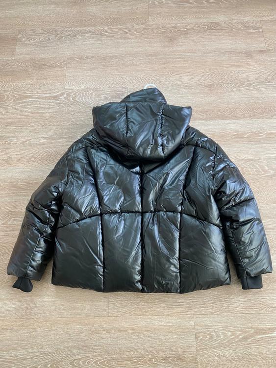 Black padded jacket with a hood, seen from behind, on a light wood floor.