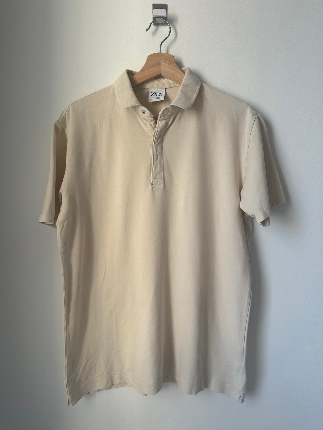 Beige polo shirt hanging on a wooden hanger against a white wall. Visible label with the text "ZVN".