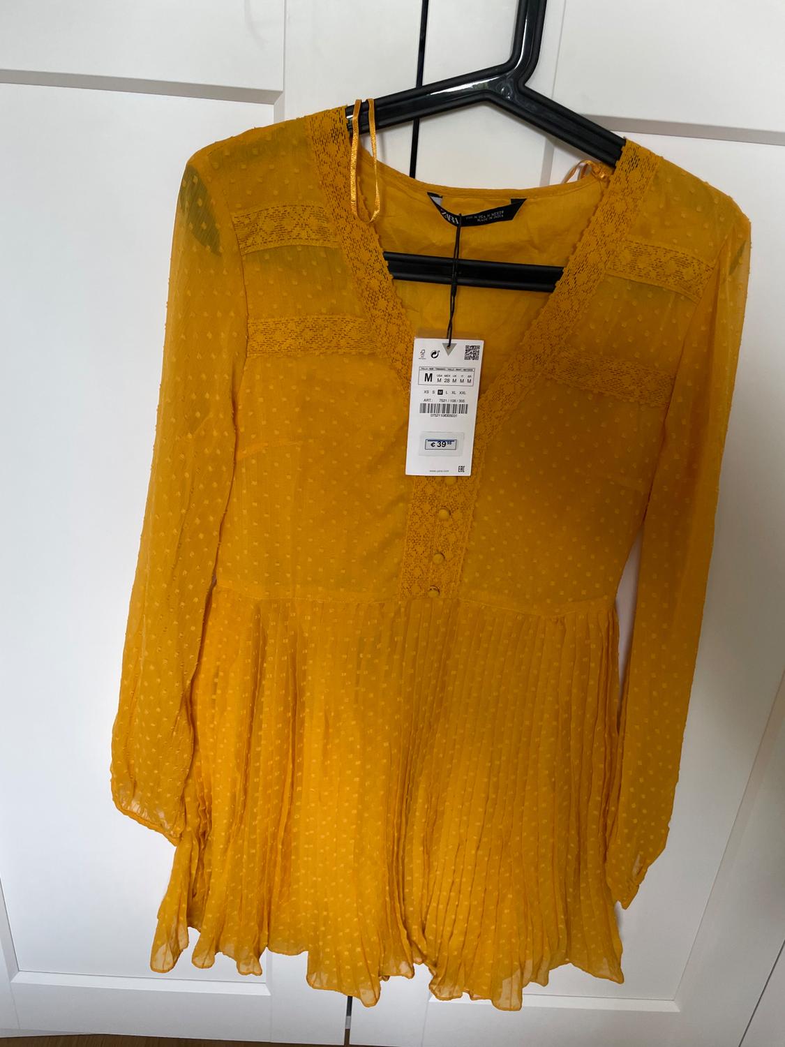 Yellow dress with a textured polka dot pattern, long sleeves, and lace details, hanging on a black hanger. Visible tag with a price of €39.99.
