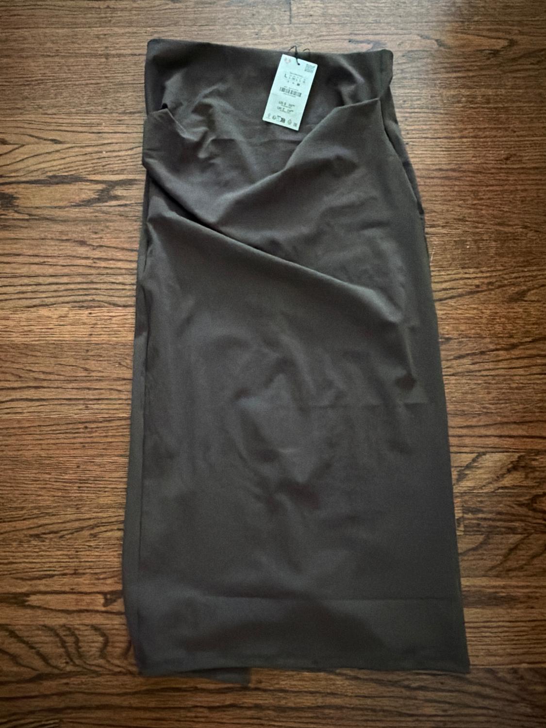 Dark gray midi skirt laid out on a wooden floor, with an attached price tag on the top.