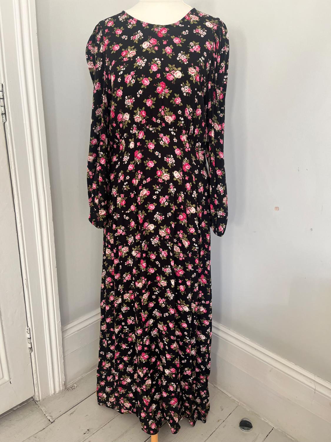 Black long dress with a floral print in pink and white tones, displayed on a mannequin on a light wooden floor.