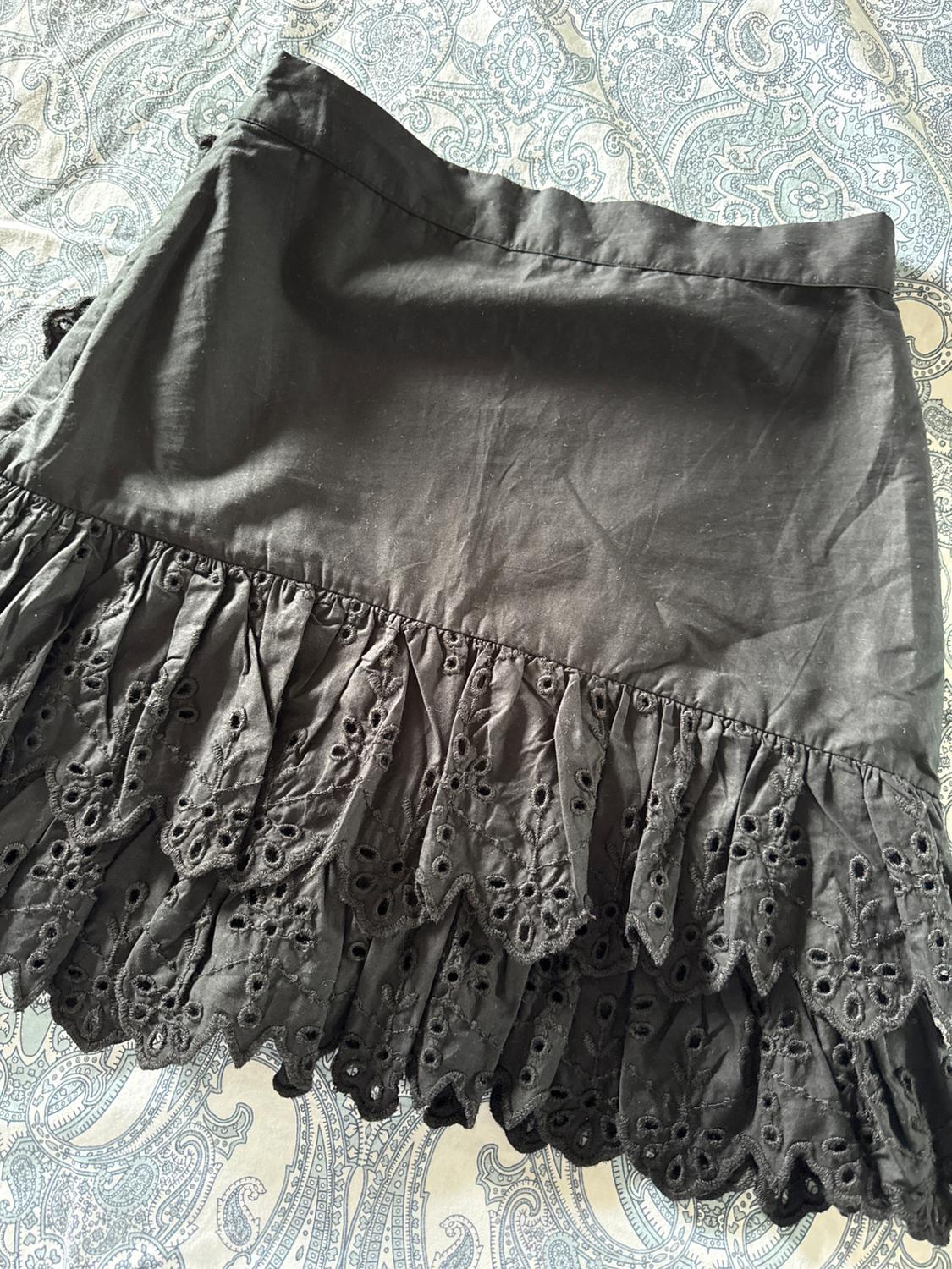 Black mini skirt with ruffles and cut-out embroidery, over a blue and white patterned fabric. Relaxed overhead composition.