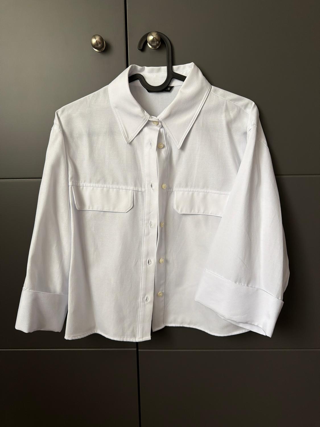 White long-sleeved shirt hanging on a black hanger against a dark grey wardrobe background.