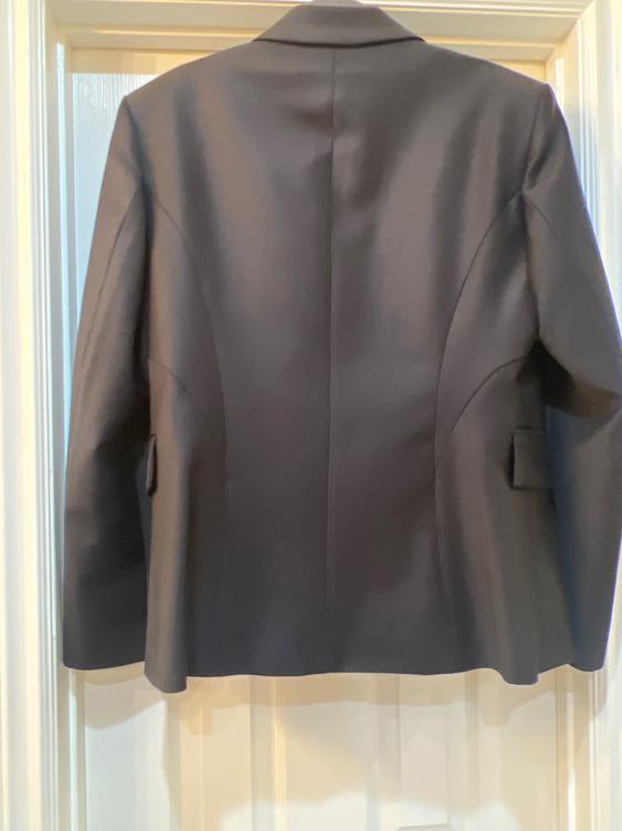 Black suit jacket hanging on a white door, viewed from the back, showing stitching details and lapels.