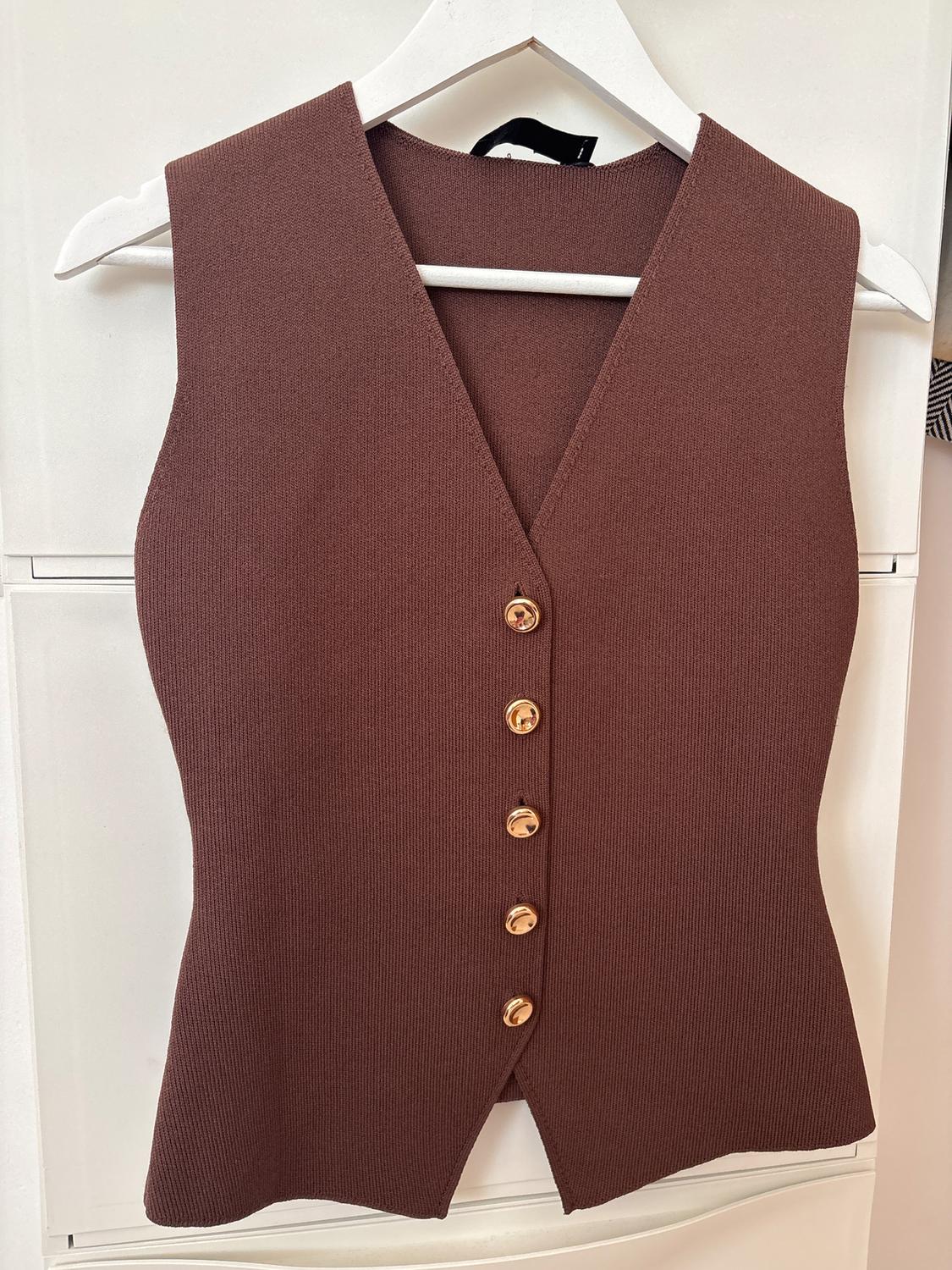 Brown sleeveless waistcoat with gold buttons, hanging on a white hanger against a light background.
