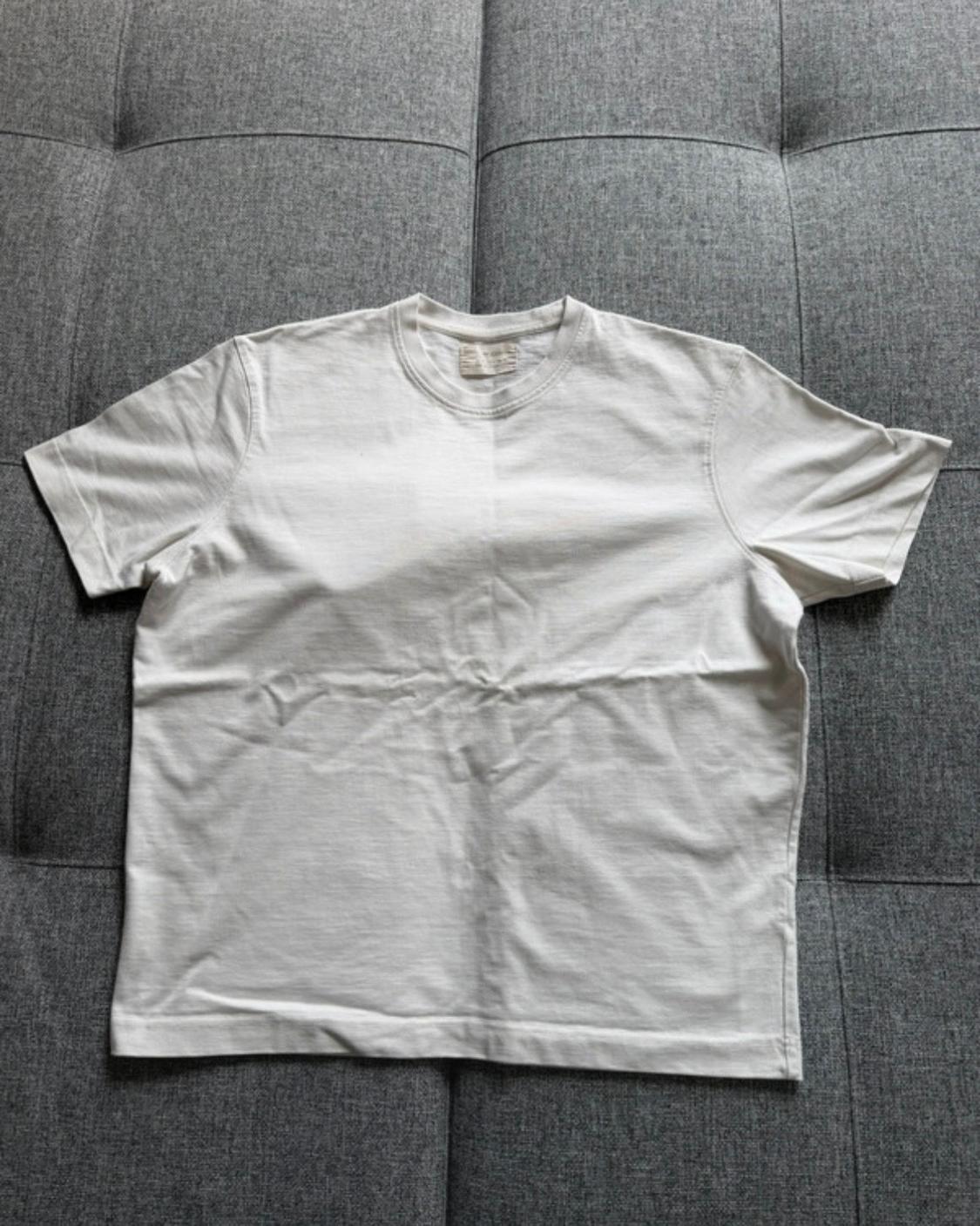 White short-sleeved, round-neck basic t-shirt, slightly creased, laid out on a textured grey sofa.