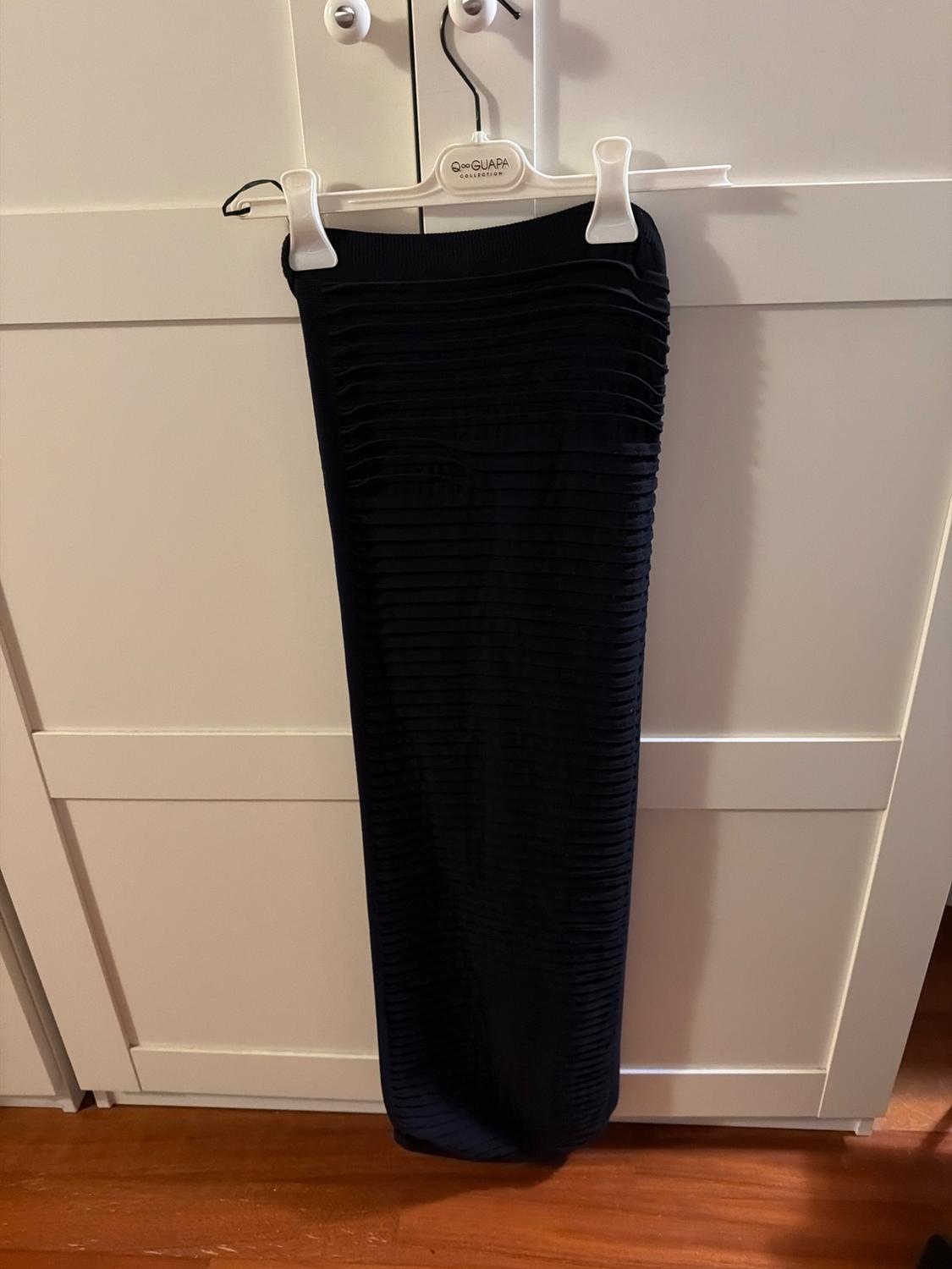 Long black skirt with horizontal line texture, hanging on a white hanger in front of a white wardrobe.