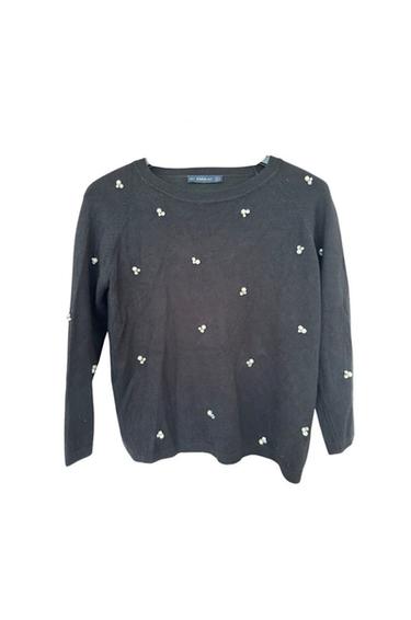 Front view of a black jumper with a detail of small white flowers scattered all over the garment.