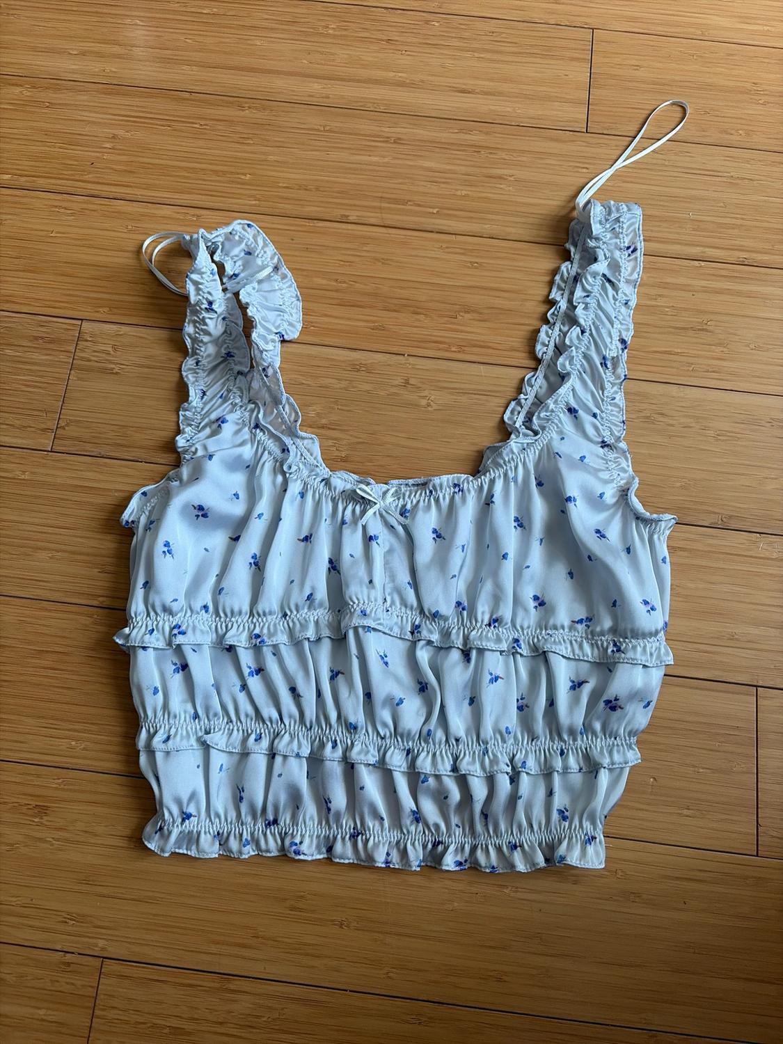 White crop top with blue flowers, straps and ruched frill bodice, and a small bow, on a wooden floor.