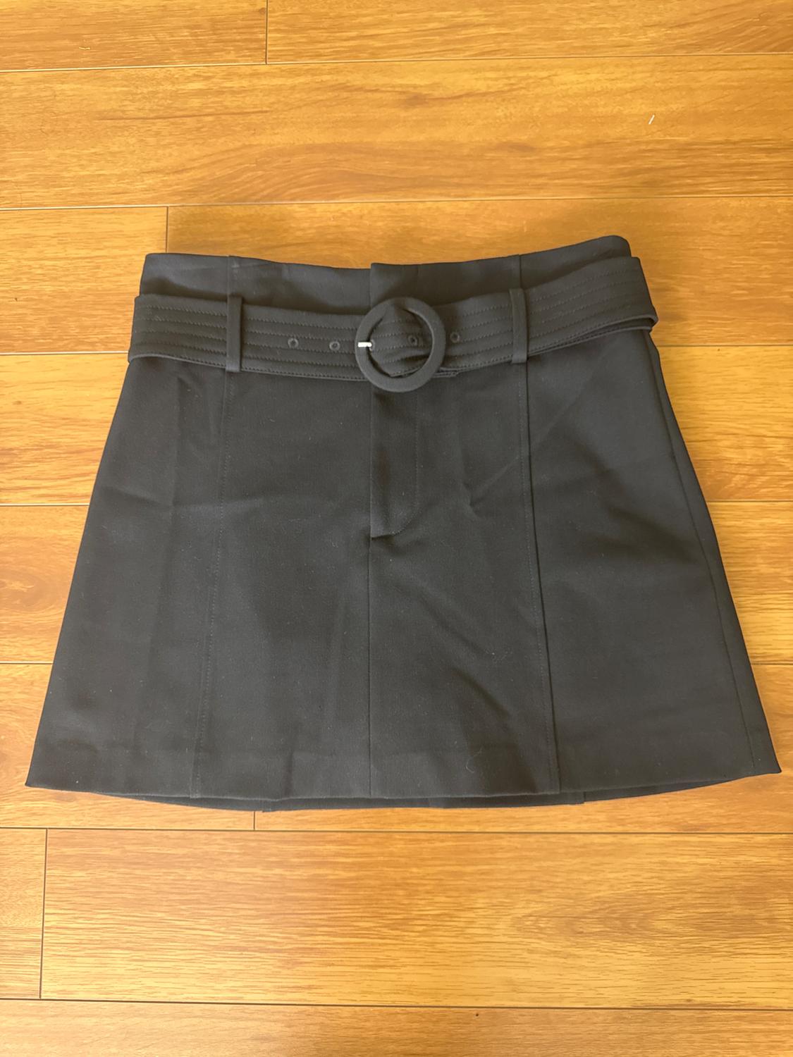 Black mini skirt with a wide belt and round buckle on a light wood background.